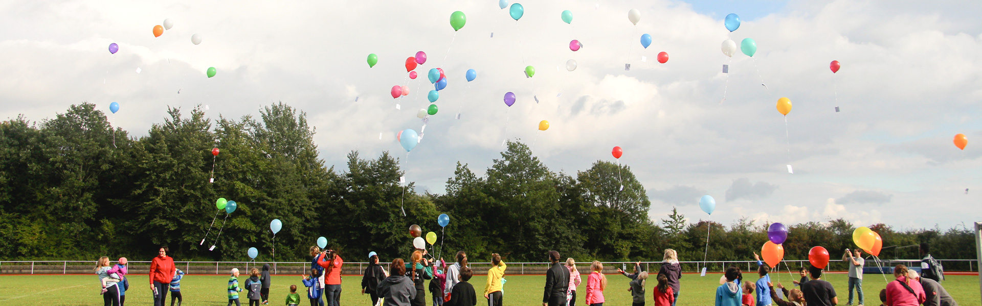 Eine Gruppe von Menschen lässt auf einem Sportplatz Luftballons in die Luft steigen.