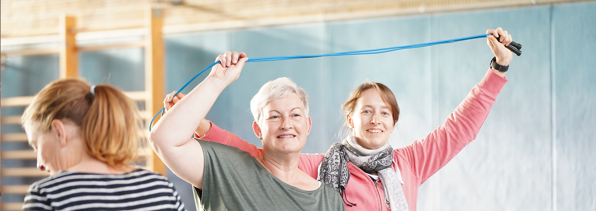 Zwei Frauen halten gemeinsam ein Seil über den Kopf und machen eine Übung.