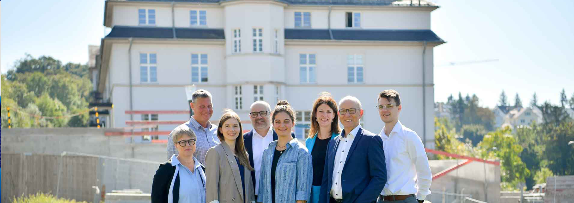 Acht Personen posieren für ein Foto draußen auf einer Wiese.