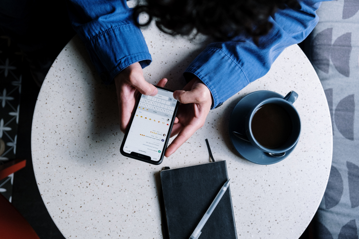 Eine Frau sitzt an einem Tisch und hat ein Smartphone in der Hand.