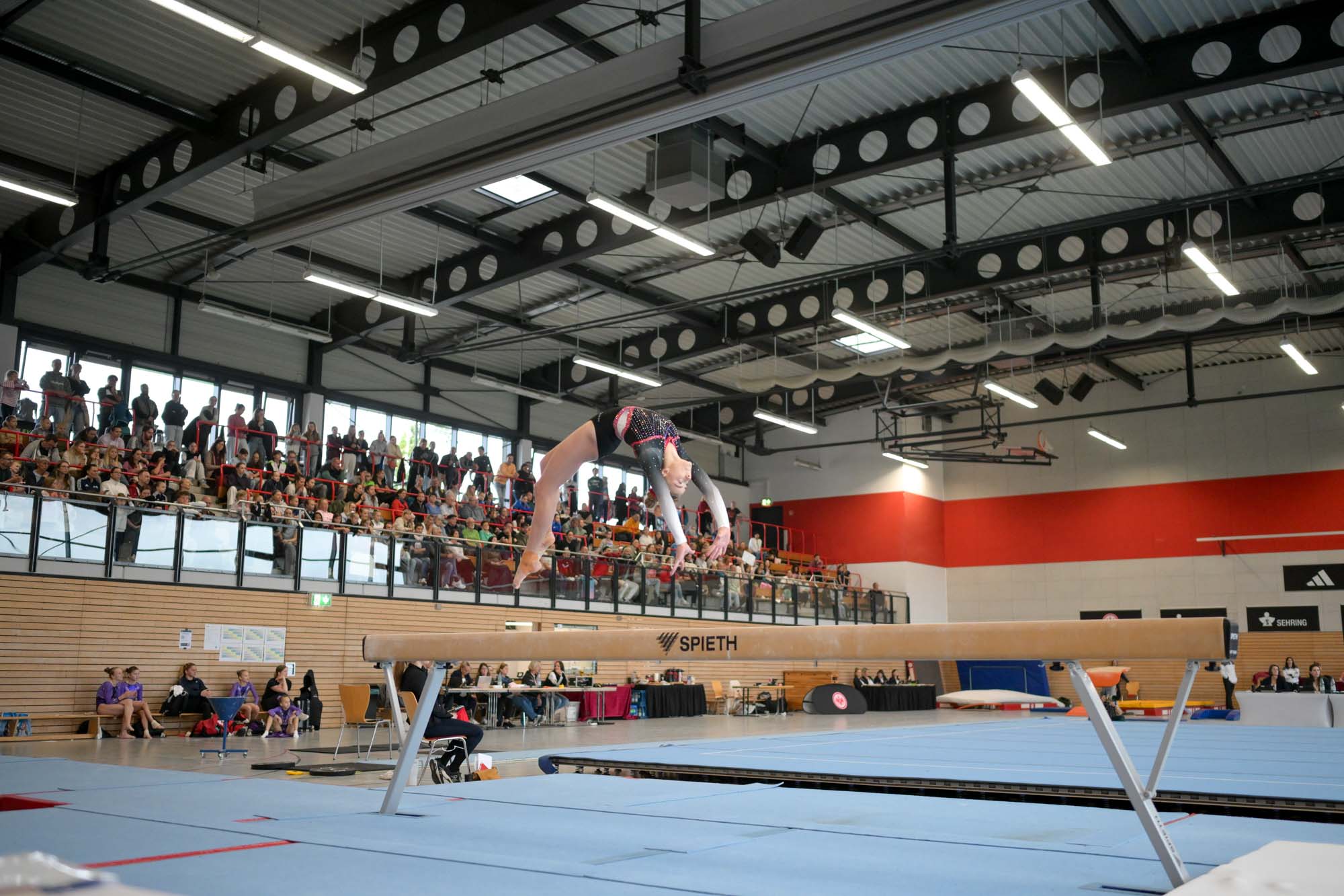 Turnen am Schwebebalken, dahinter die Halle zu erkennen